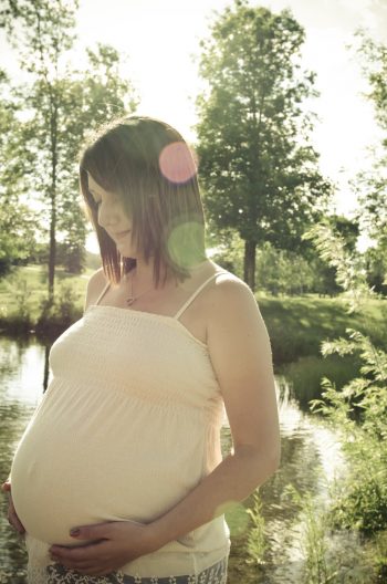 Woman beside a lake looking down at her pregnancy